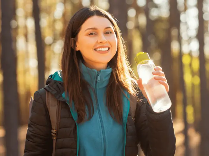 woman drinking water while hiking - best way to carry water while hiking